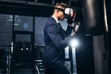 side view of businessman in suit and virtual reality headset boxing in gym