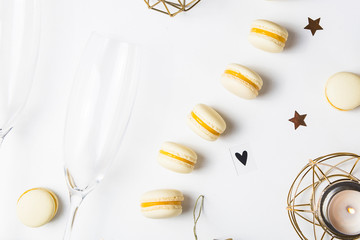 Yellow lemon macaroons on a white background next to champagne glasses. Festive gourmet Christmas aperitif. Top view, flat lay
