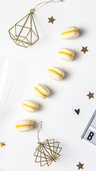 Yellow lemon macaroons on a white background next to golden Christmas decorations and asterisks. Festive tender French dessert. Top view, flat lay
