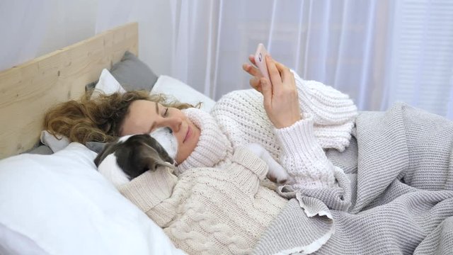 Young Woman Using Mobile Phone On Bed With Her Cute Dog