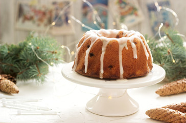 Pie with raisins and icing from powdered sugar on the background of fir branches and garlands. Rustic style.
