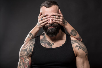Uomo muscoloso e tatuato in primo piano e mani  tatuate che gli coprono gli occhi
