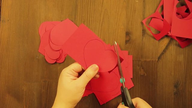 The girl cuts hearts of various sizes from red cardboard. Time laps