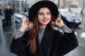 Young fashion woman walking on the city street wear black hat look around and smile to camera. Copy space. - Image
