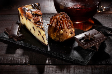 Anthill cake and cheese cake with chocolate and condensed milk next to cup of tea on a wooden table. Low key.