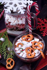 Hot chocolate with marshmallows and pretzels in a cup and a dry mix for preparing the drink in a glass jar