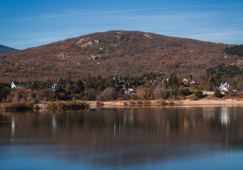 Houses between trees in front of a lake