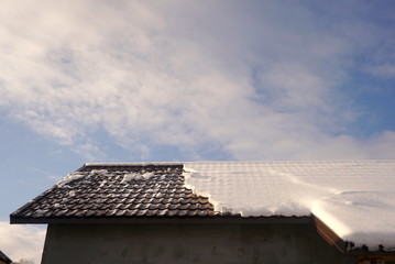 Snow on the roof of the house against the blue sky 