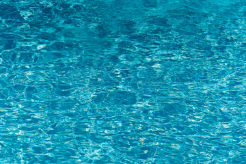 Blue water in swimming pool background. Ripple Water in swimming pool with sun reflection. Blue swimming pool rippled water detail.