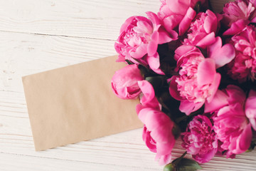 lovely pink peonies with empty craft card on rustic white wooden background top view, space for text. floral greeting card mock-up. beautiful flowers. happy mothers day concept