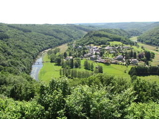 green landscape in the flemish ardennes with a village, a river and a green hill with pines