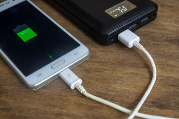 Powerbank and mobile phone on a wooden table, power bank charging, green battery