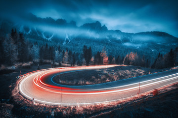 Wazig autokoplampen op kronkelende weg in bergen met lage wolken & 39 s nachts in de herfst. Humeurig landschap met asfaltweg, lichte paden, mistig bos, rotsen en blauwe lucht in de schemering. Rijbaan in Italië