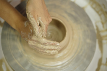 woman makes a jug with dirty arms on a Potter's wheel from raw wet clay
