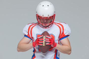 American football sportsman player wearing helmet holding rugby ball isolated on grey background