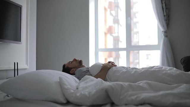 Man wake up in early morning on his bed, stretching arms