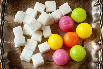 Candy balls and pieces of sugar. Colored dragees hard fruit candy and sugar stacked on a silver saucer, wooden background. The concept of sweet life.