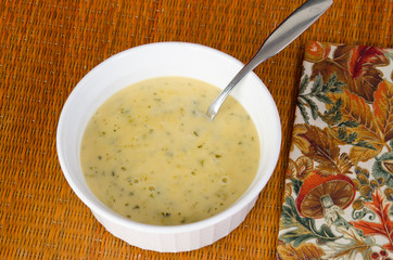 Bowl of Cheese and Broccoli Soup on Bamboo Mat with Autumn Scene on Napokin