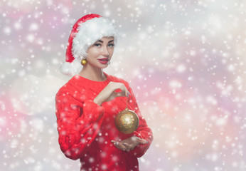 Portrait of a beautiful woman in a red  Santa Claus hat and knitted red sweater holding a golden christmas ball on snowflakes background. New Year's concept.