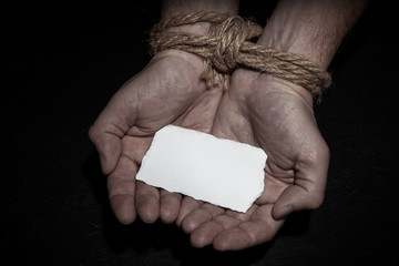 Man with his hands tied with a rope is holding an empty piece of paper. Slavery concept, please...