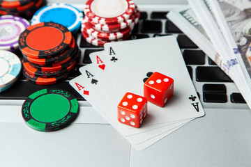 Online casino laptop. Laptop keyboard and chips with dice and playing cards and money cash dollars on green gaming table. Game addiction gambling. Poker online