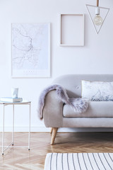 Minimalistic scandinavian white interior with design sofa, poster, coffee table, cozy blanket,and mock up frames. White background walls and modern triangle lamp. 