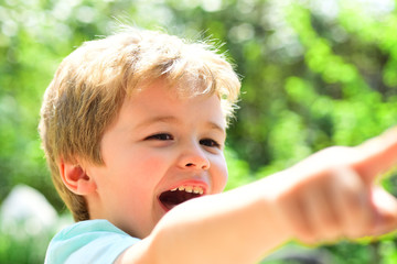 Happy child with big smile. Boy showing, kid holding his hand up and pointing. Cute kid portrait. Happy childhood and sunny day. Handsome boy enjoying happiness. Funny face.