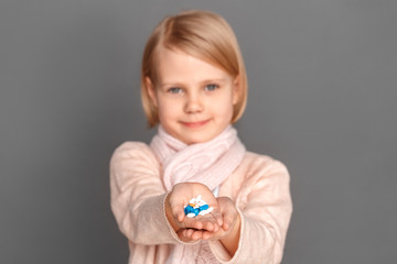 Freestyle. Little girl in scarf isolated on grey giving pills to camera close-up smiling happy blurred