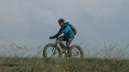 Fat bike also called fatbike or fat-tire bike in summer driving through the hills. The guy is riding a bike along the sand and grass high in the mountains. He performs some tricks and runs dangerously