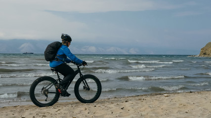 Fototapeta na wymiar Fat bike also called fatbike or fat-tire bike in summer driving on the beach. The guy is going straight on the beach. On the sand on such a bike ride is not difficult.