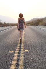 Fototapeta premium Woman walking down desert road during sunrise