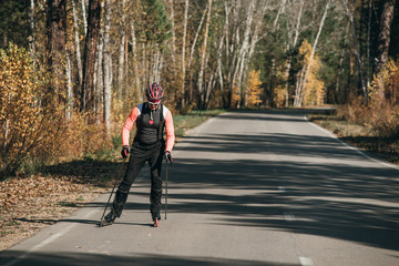 Training an athlete on the roller skaters. Biathlon ride on the roller skis with ski poles, in the helmet. Autumn workout. Roller sport. Adult man riding on skates.