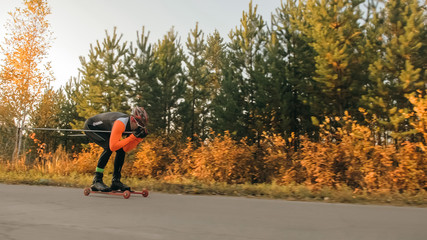 Fototapeta premium Training an athlete on the roller skaters. Biathlon ride on the roller skis with ski poles, in the helmet. Autumn workout. Roller sport. Adult man riding on skates.
