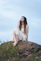 Beautiful girl sitting on a rock in a light dress.