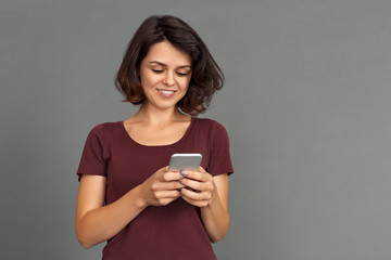 Freestyle. Young woman isolated on grey typing message on smartphone joyful