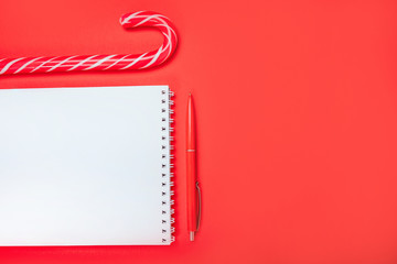 Christmas flatlay with clean spring pad, red pen and candy canes on the bright red background.