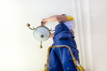 Worker in workwear is installing a chandelier and connects it  to electricity on the ceiling from...