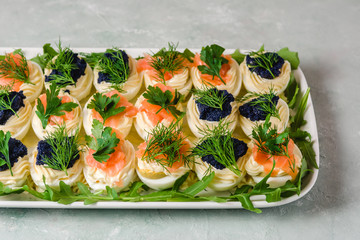 Stuffed eggs with salmon and caviar decorated by parsley, dill and arugula. Party food