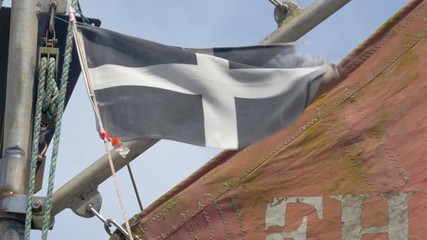 The Cornish Saint Piran's Flag flying in the wind atop the mast of a fishing boat in Cadgwith Cove, Cornwall.