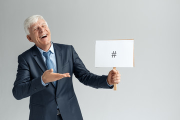 Business Lifestyle. Businessman standing isolated on gray showing board with hash sign laughing...