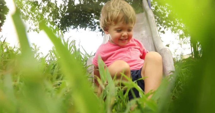 From below of little boy on slide in green grass having fun on playground
