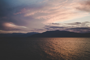 abstract evening twilight time after sunset outdoor landscape view with dark mountain ridge silhouettes shape near sea calm water surface wallpaper pattern unfocused concept