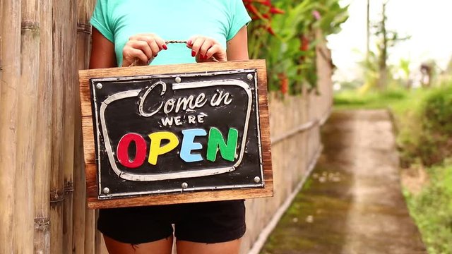 Open sign board in a woman hands on a tropical nature background. Shooted on Bali island, full HD.