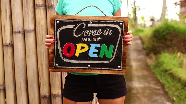 Open sign board in a woman hands on a tropical nature background. Shooted on Bali island, full HD.