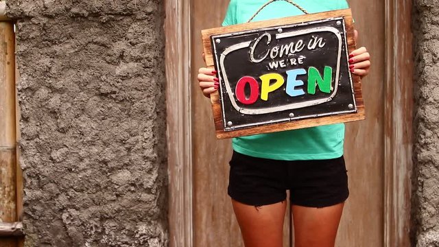 Open sign board in a woman hands on a tropical nature background. Shooted on Bali island, full HD.