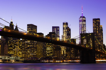 Fototapeta na wymiar Beautiful Brooklyn Bridge and the illuminated Manhattan's skyline at dusk with dark blue sky and smooth water surface. Picture taken from the Brooklyn district, New York, USA.