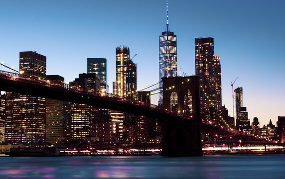 Beautiful Brooklyn Bridge and the illuminated Manhattan's skyline at dusk with dark blue sky and smooth water surface. Picture taken from the Brooklyn district, New York, USA.