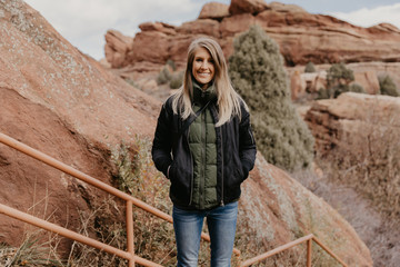 Young Beautiful Modern Caucasian Woman Smiling While Traveling to Red Rocks Park in United States Outside in Nature at the State Park with Ancient Stone and Blue Sky Background