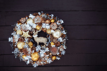 Top view Beautiful hand made golden Christmas wreath decorated with pine cones, ornamentals, spruce branches, balls, stars and decorative deer on black wooden background, flat lay. Copy space.