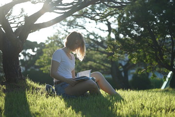 caucasian blonde woman reading book on the grass